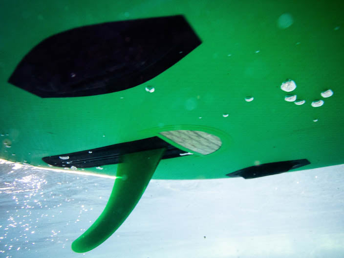 Underwater view of a Hala StompBox fin on the bottom of a green paddle board
